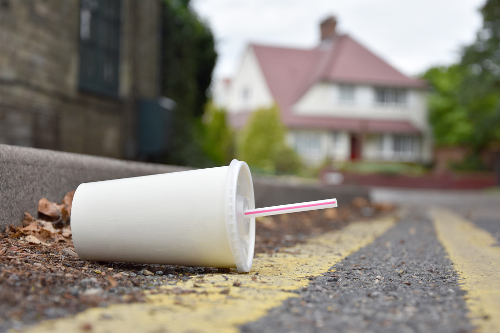 A carelessly discarded drink or soda container with drinking straw lies in the gutter of an urban street