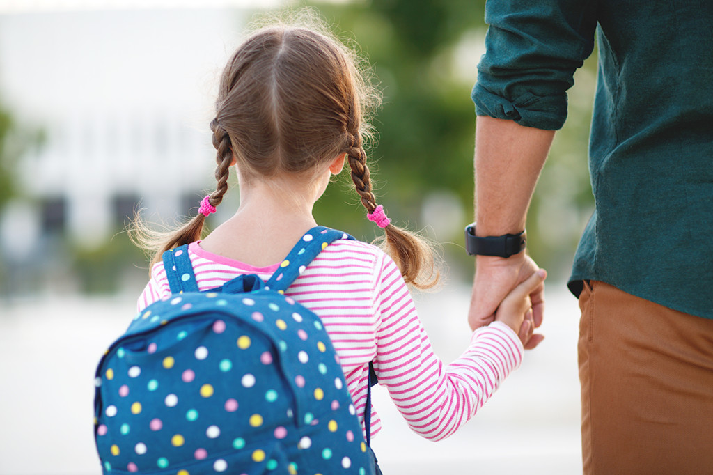 first day at school. father leads a little child school girl in first grade