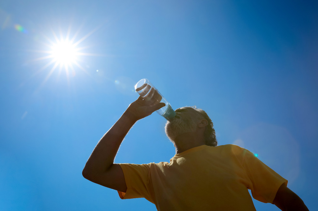 Senior man drinking water to prevent heat stroke outdoors, low angle view