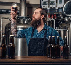 Portrait,Of,Tattooed,,Bearded,Hipster,Male,Manufacturer,Tasting,Beer,In