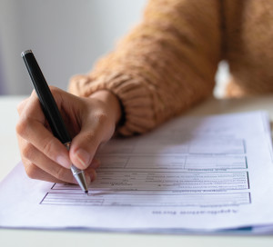 Close-up of lady filling application form. Unrecognizable woman in sweater sitting at table and preparing her resume. Job search concept