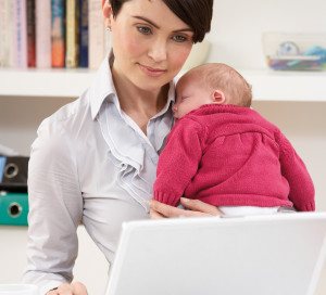 Woman With Newborn Baby Working From Home Using Laptop