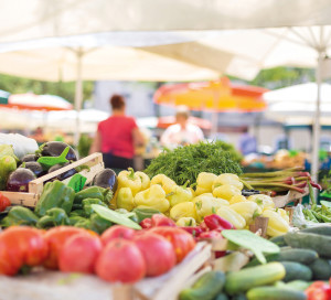 Farmers' food market stall with variety of organic vegetable. Vendor serving and chating with customers.
